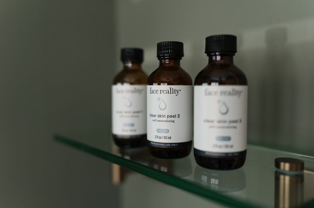 Three amber 'Face Reality' clear skin peel bottles on a glass shelf, center bottle in focus