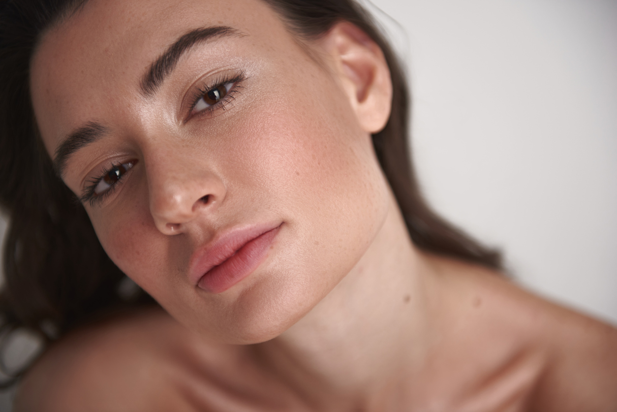 Close-up beauty portrait of a woman with natural makeup, clear glowing skin, neutral background