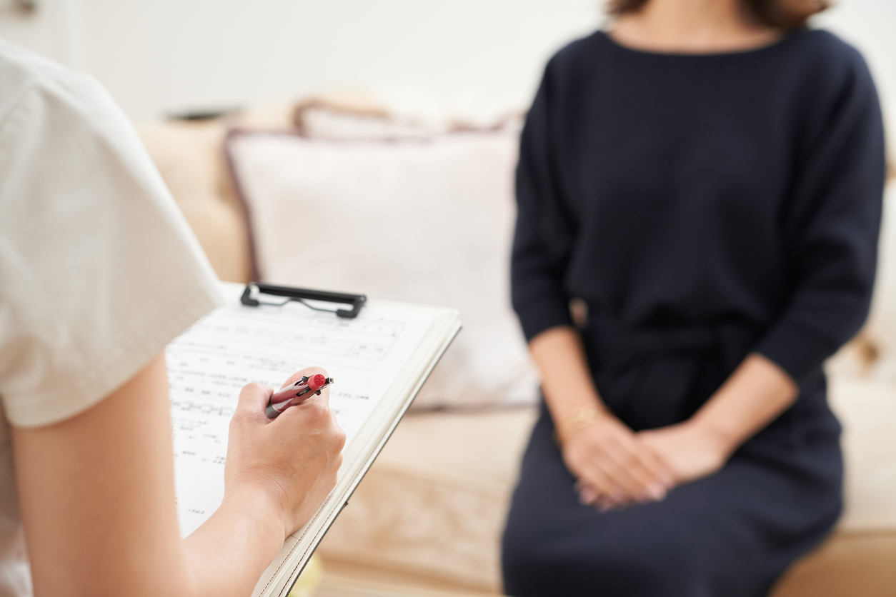 Therapist taking notes on a clipboard during a counseling session with a woman seated on a couch