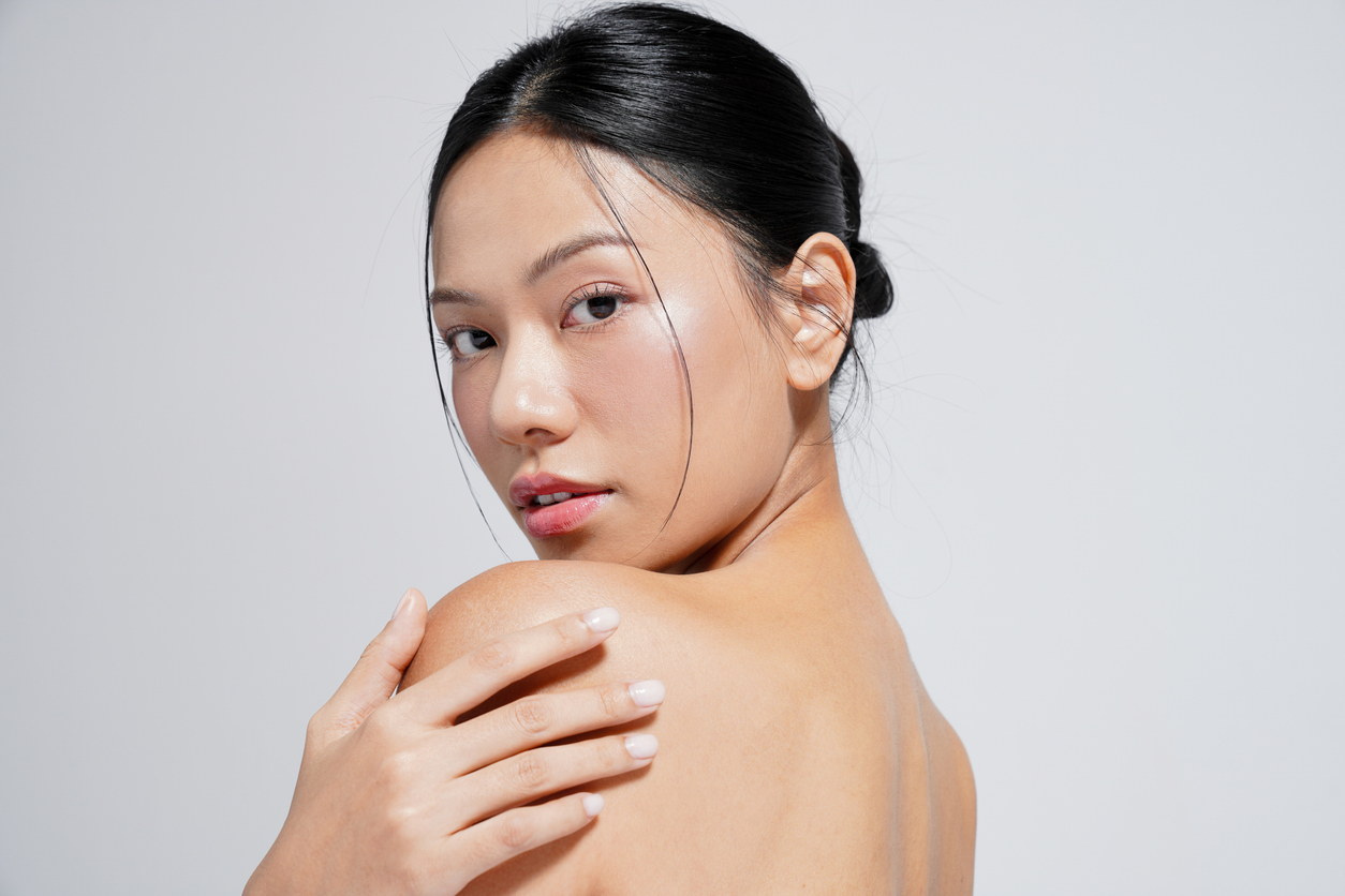 Portrait of a woman with glowing skin, natural makeup, looking over her shoulder, hand on bare shoulder, skincare