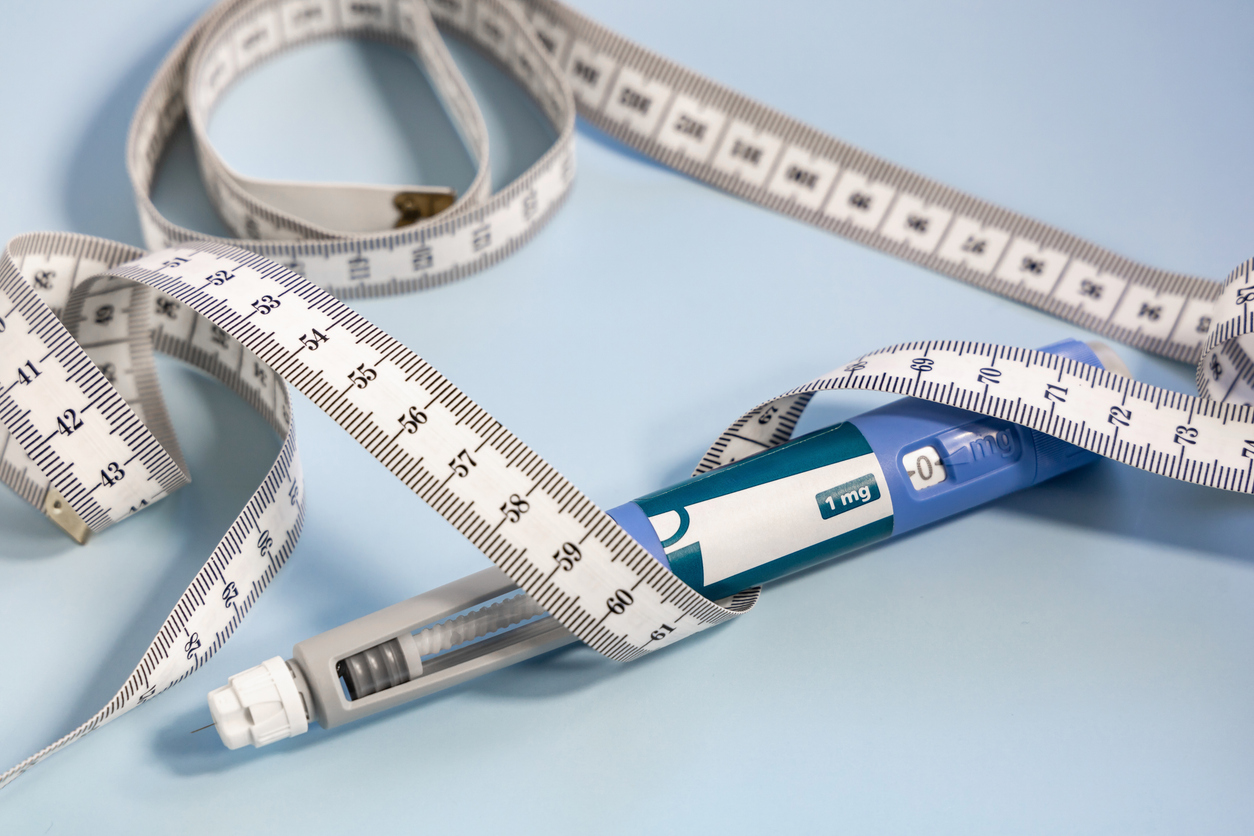 Insulin injection pen wrapped in a measuring tape on a light blue background, symbolizing diabetes and weight management